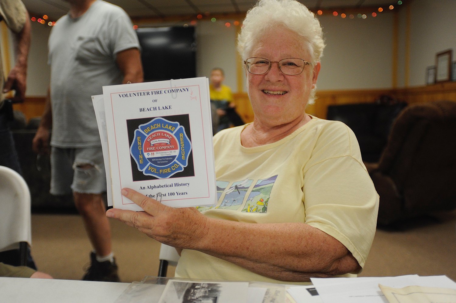 Carol Henry Dunn, Berlin Township historian and chronicler of events at the Volunteer Fire Company of Beach Lake, displays a mock-up of the 100th Anniversary souvenir pamphlet, just a few days before it went to press.